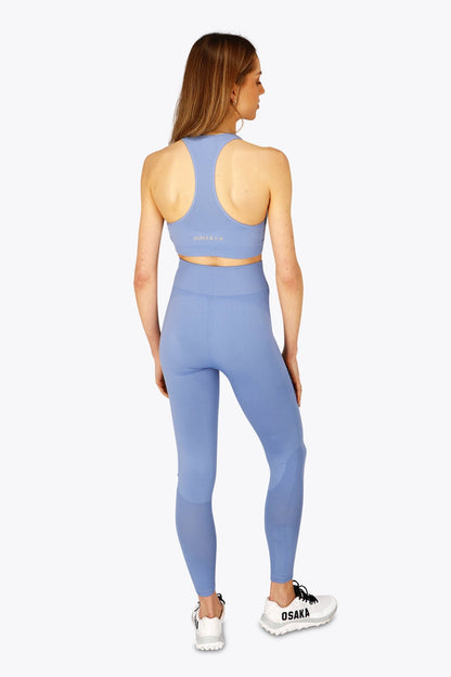 Woman wearing the Osaka women tech sports bra in manor blue with logo in grey. Back view