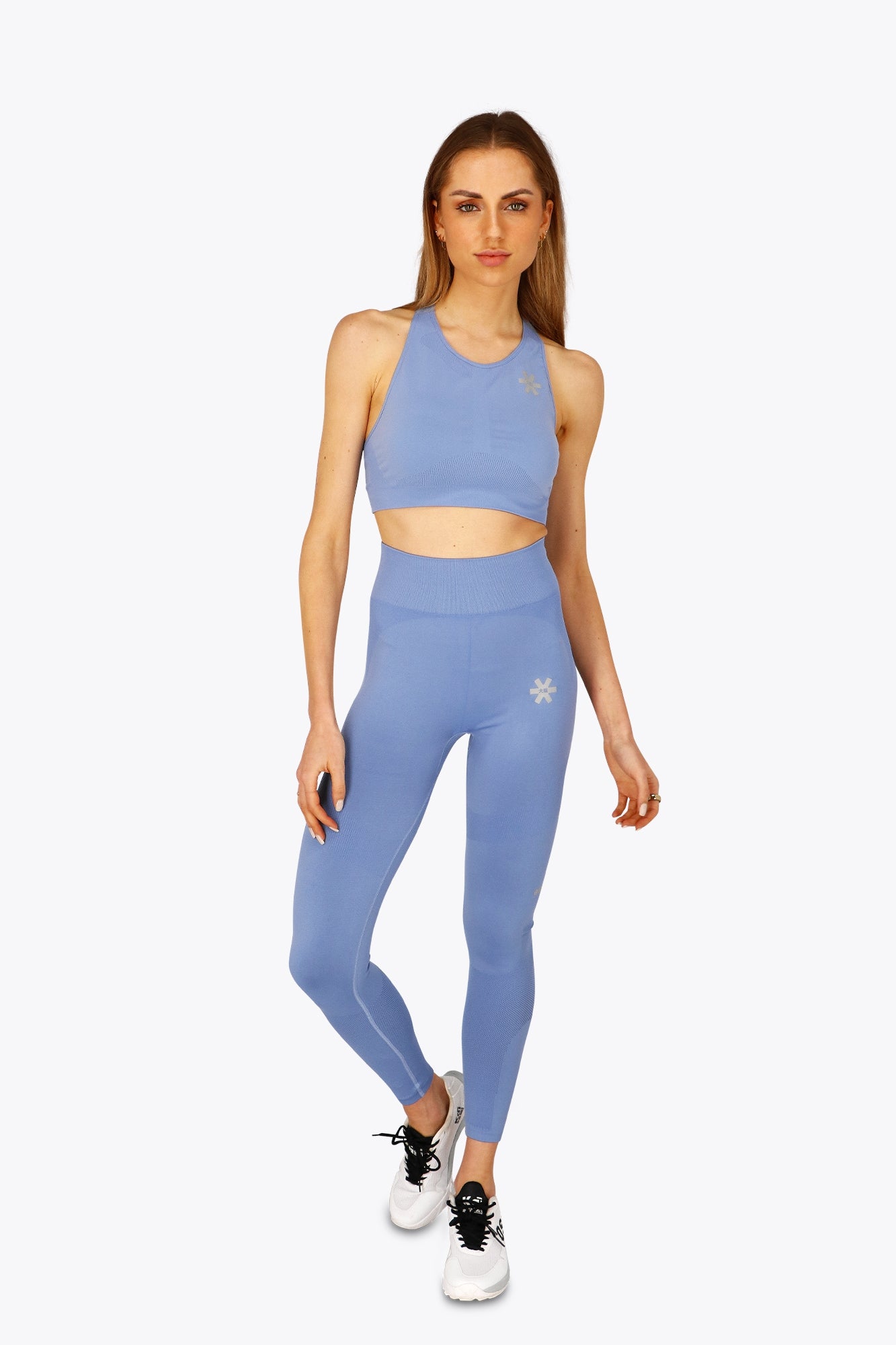 Woman wearing the Osaka women tech sports bra in manor blue with logo in grey. Front view