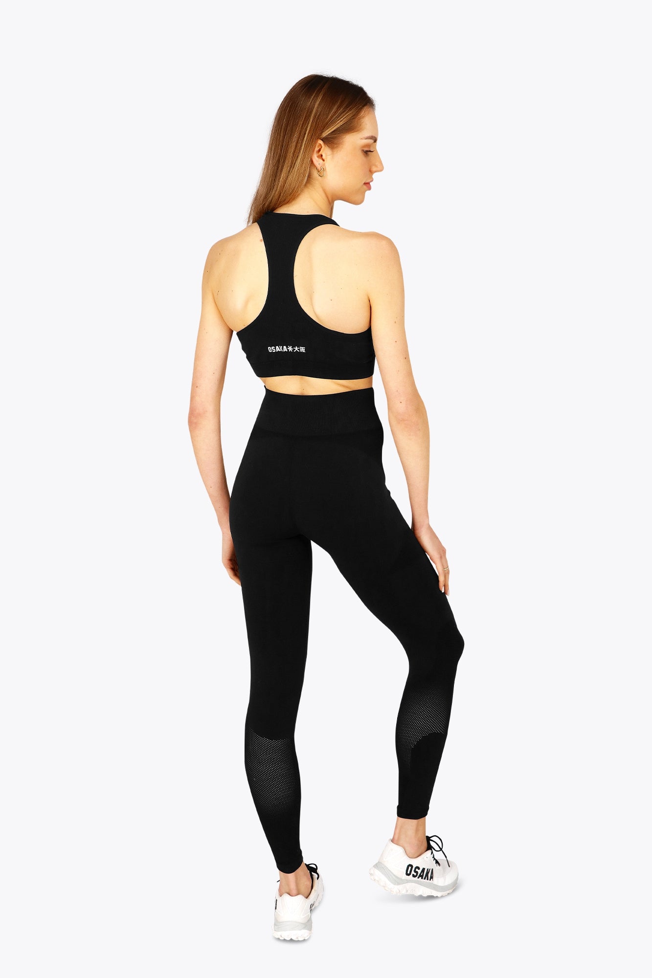 Woman wearing the Osaka women tech sports bra in black with logo in grey. Back view