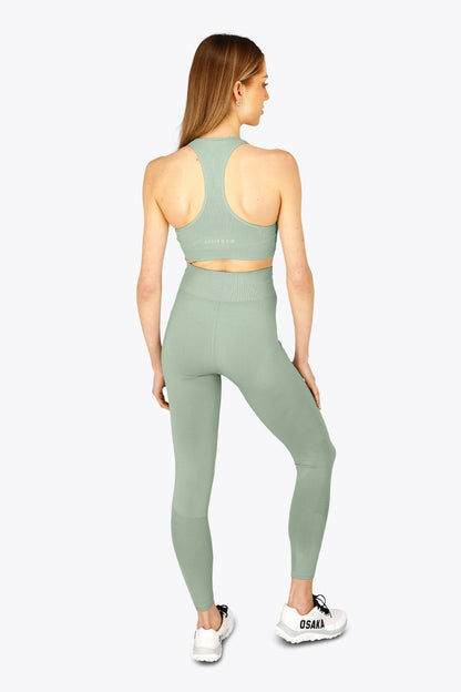 Woman wearing the Osaka women tech sports bra in jadeite with logo in grey. Back view