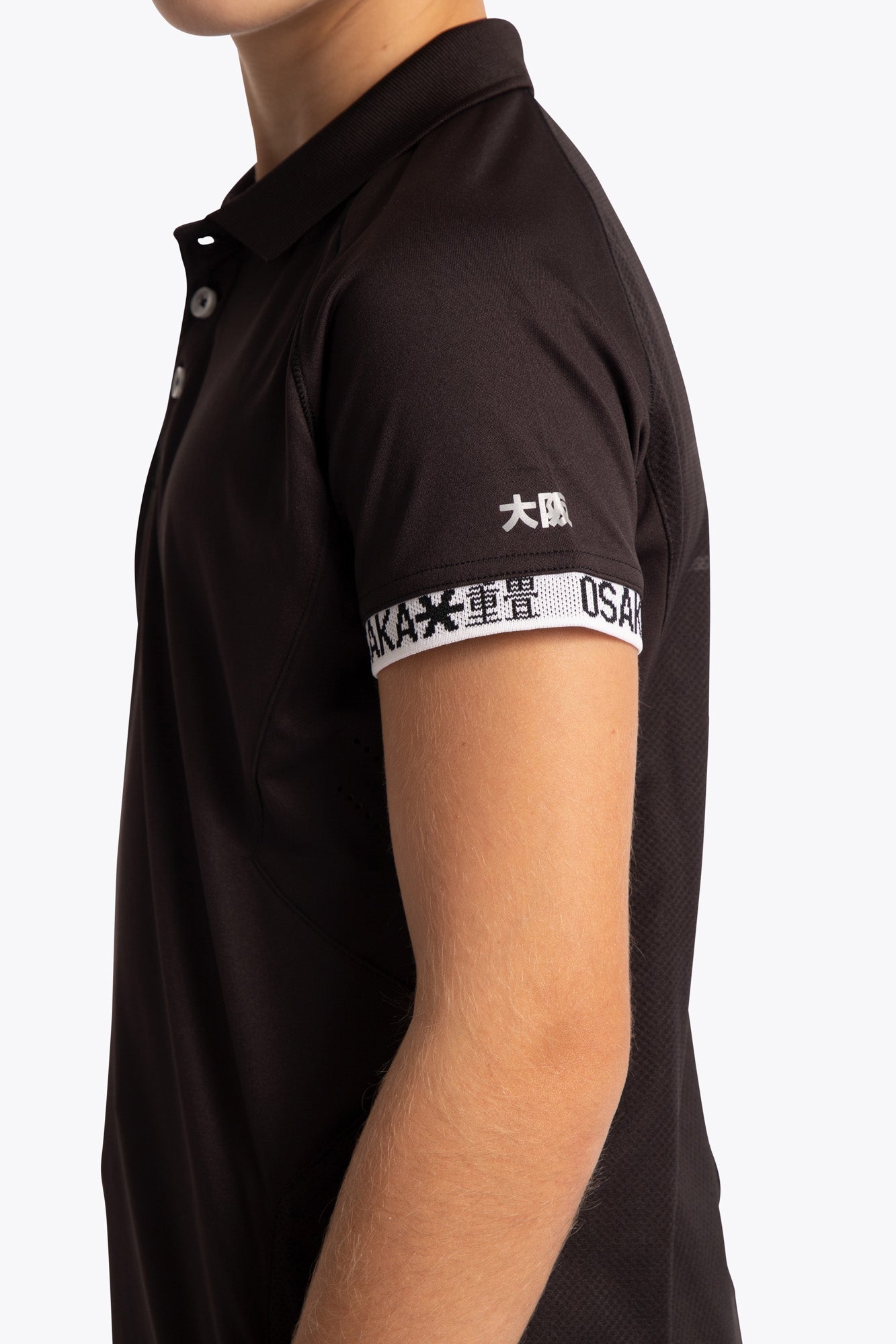 Boy wearing the Osaka Kids Polo Jersey in Black. Side view