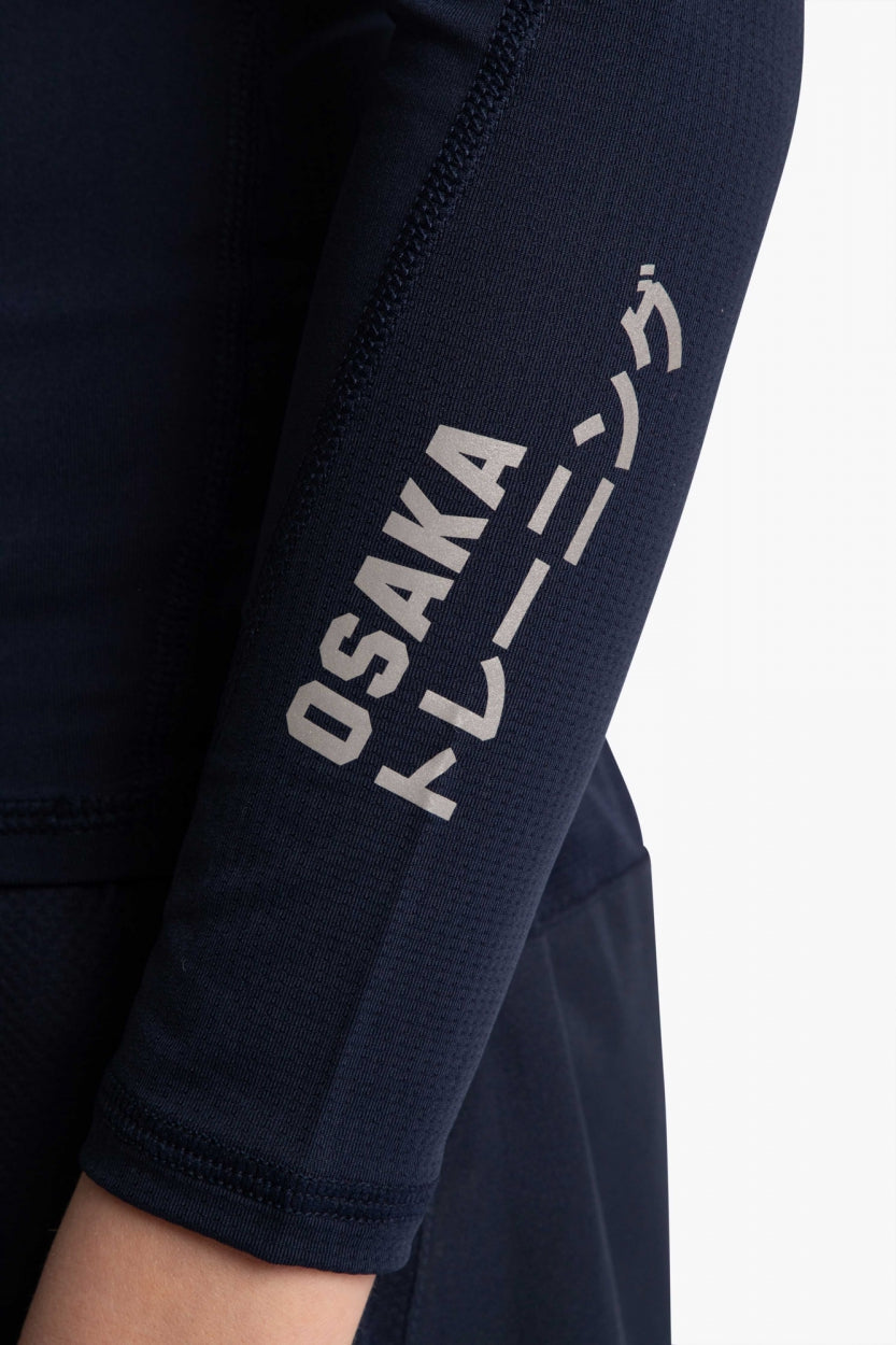 Model wearing the Osaka Kids Baselayer Top in Navy. Front detail logo sleeve view