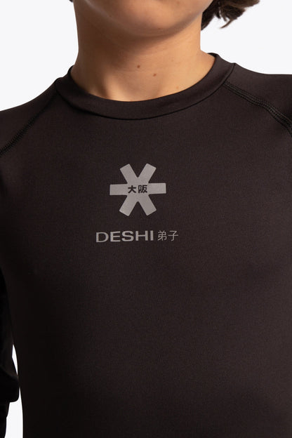 Kid wearing the Osaka Kids Baselayer Top in Black. Front detail logo view