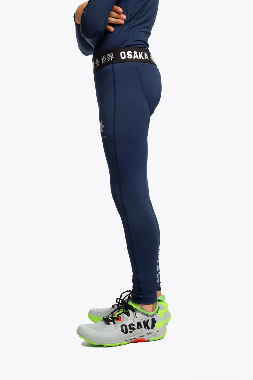 Model wearing the Osaka Kids Baselayer Tights in Navy. Side view