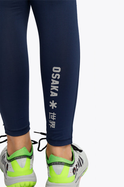 Model wearing the Osaka Kids Baselayer Tights in Navy. Detail logo view